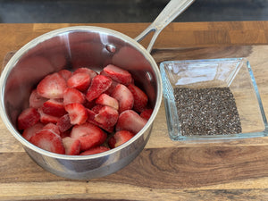 Frozen strawberries in a saucepan beside a dish of chia seeds, the two ingredients for strawberry chia jam